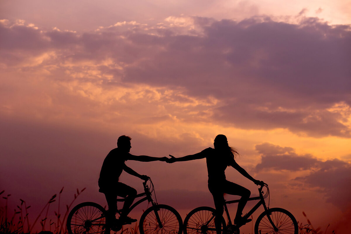 A man and a woman sitting on bicycles, holding hands