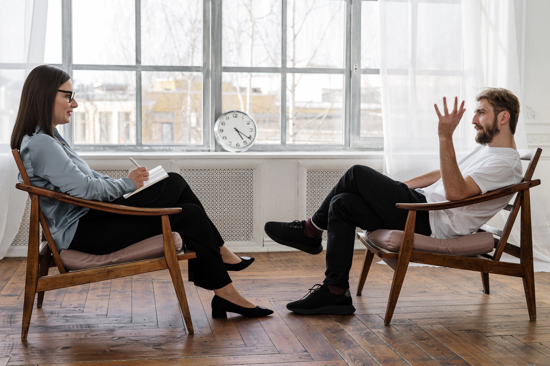 a man and woman sitting in chairs talking to each other