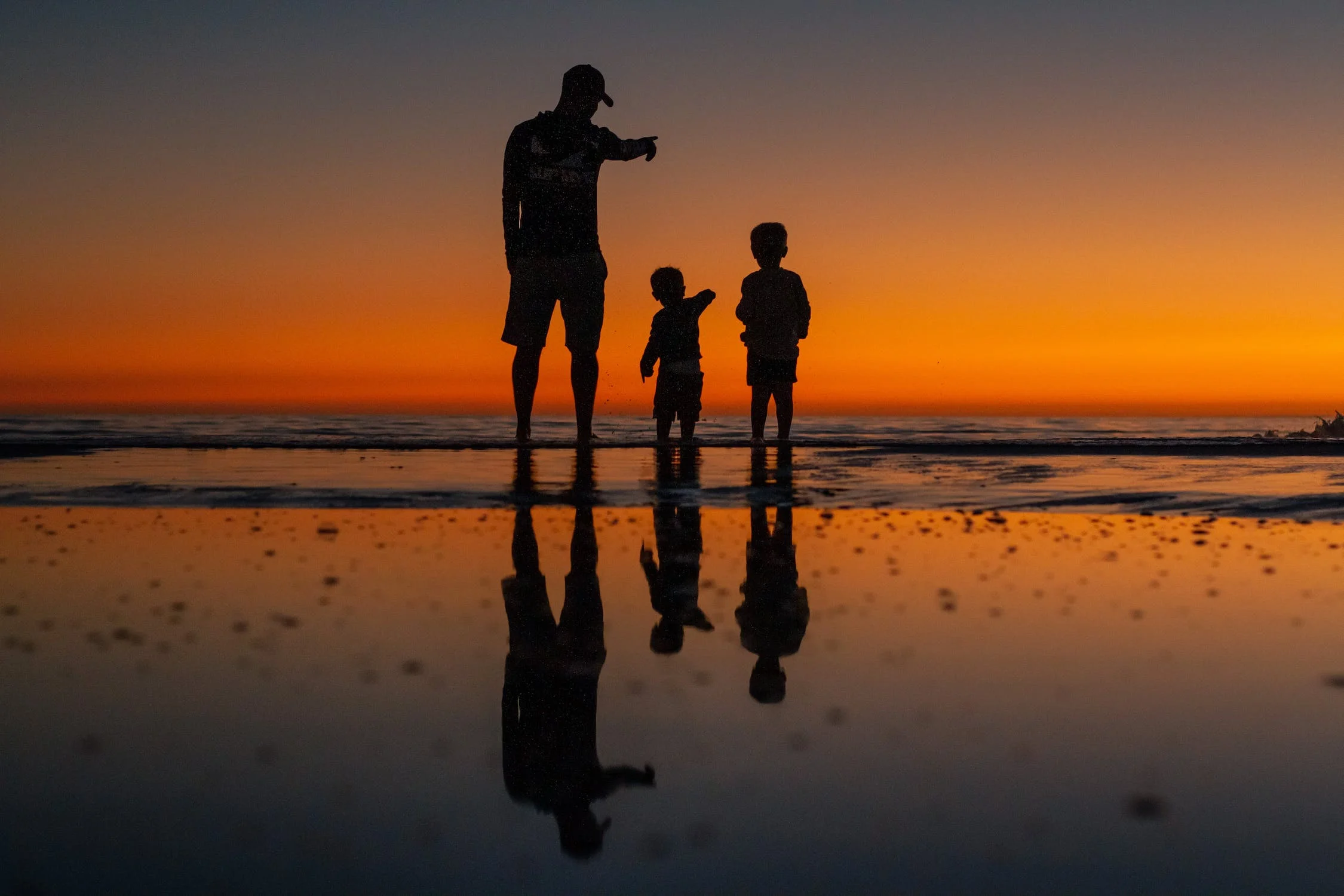 a man and two children standing on the beach at sunset